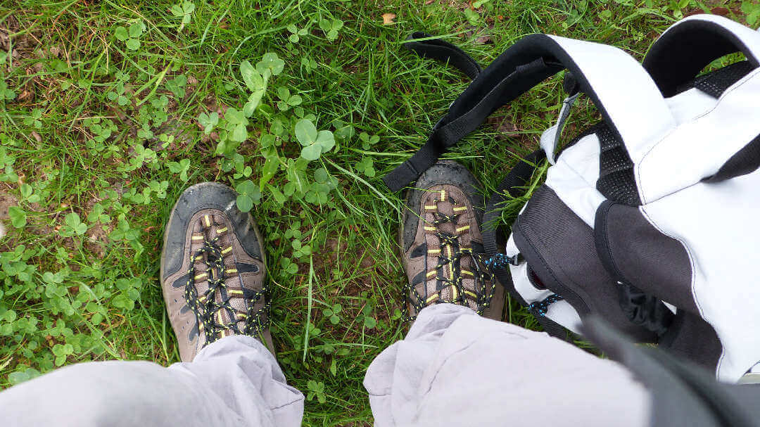 Photo en plongée de chaussures et d'un sac de randonnée sur fond d'herbe